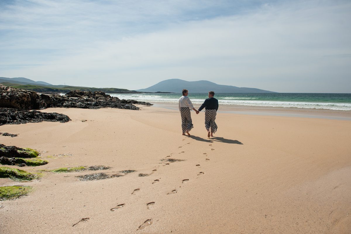 Couple walking hand in hand leaving footprints in the sand at Borve beach, Isle of Harris